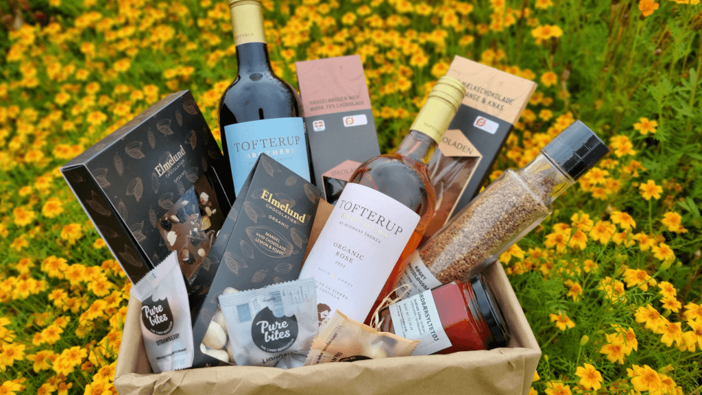 A gift basket with specialties from the Tinnetgaard farm shop placed in a flower meadow
